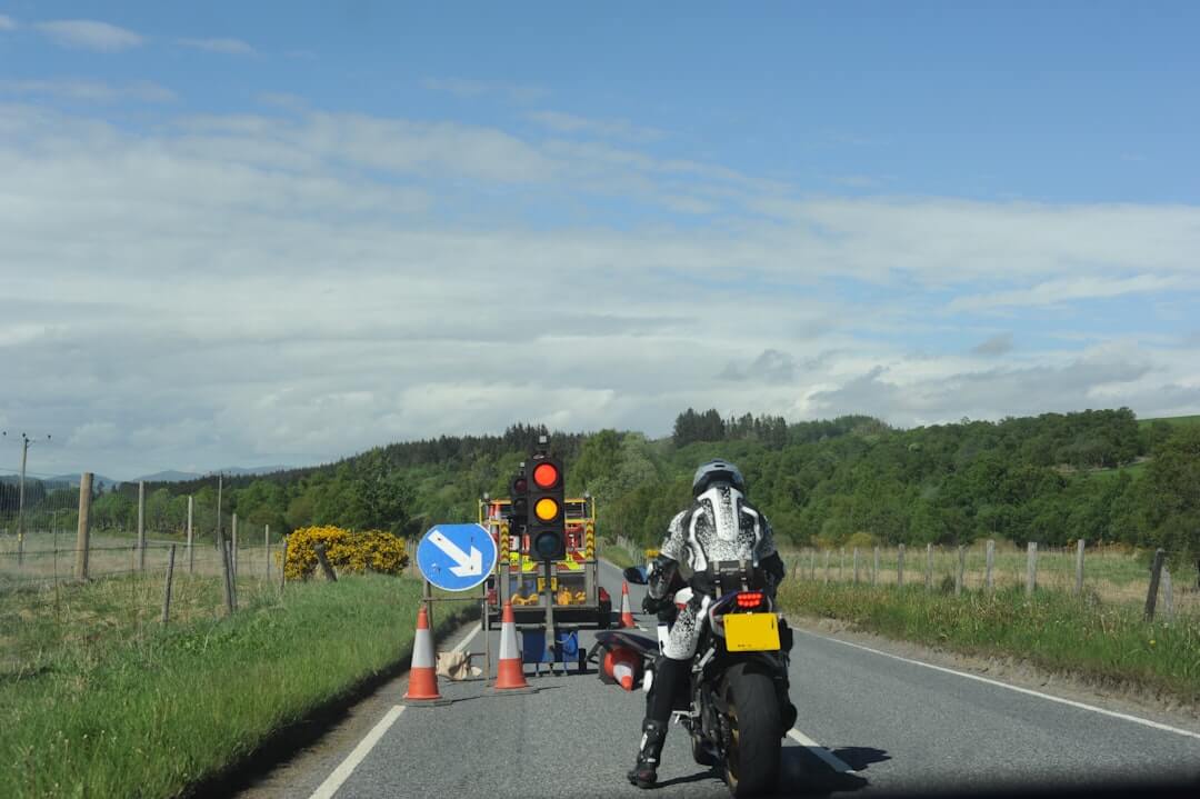 Motorcyclist stopped at red temporary traffic light on rural road.