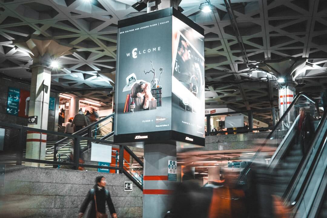 Digital billboard in a busy metro station with escalators.
