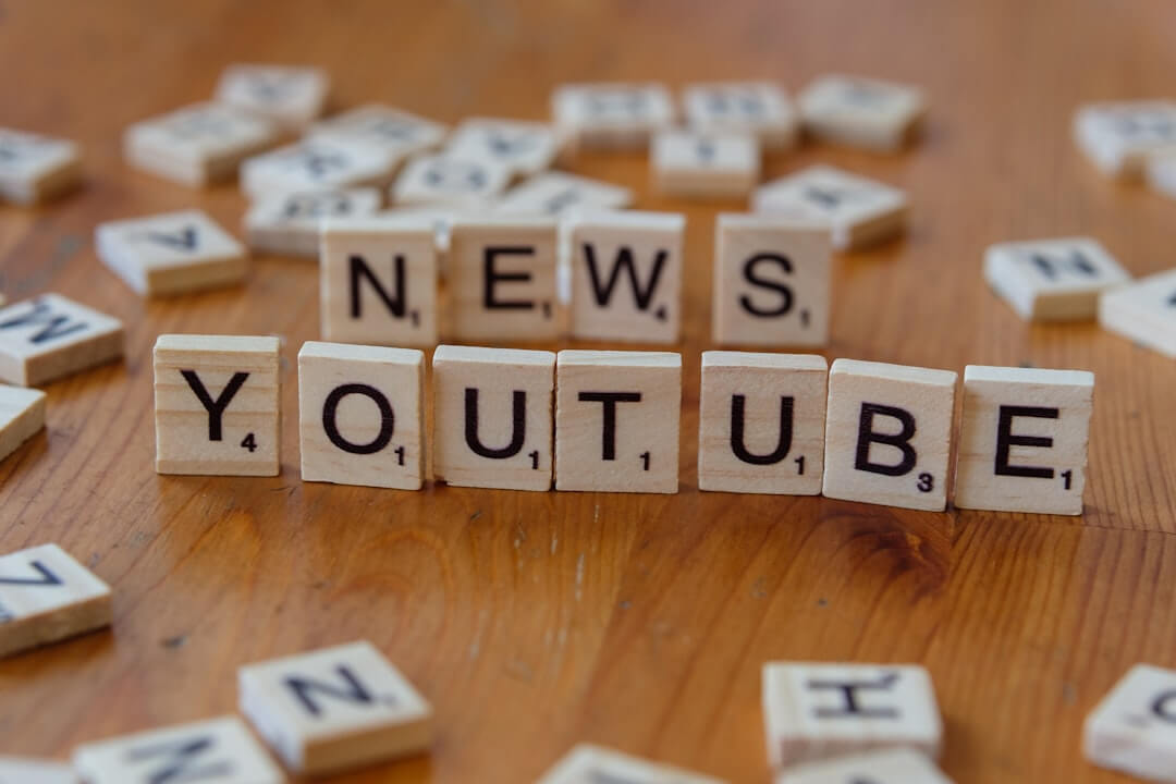 A wooden table topped with scrabble tiles spelling news and youtube