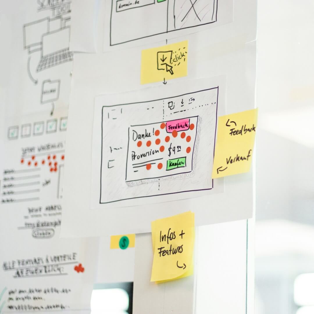 Hand-drawn website wireframes with yellow sticky notes on a glass office wall