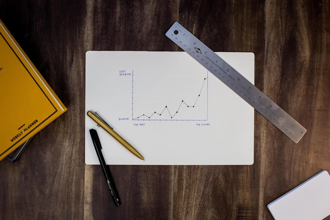 A hand-drawn line graph on paper with a metal ruler and two pens