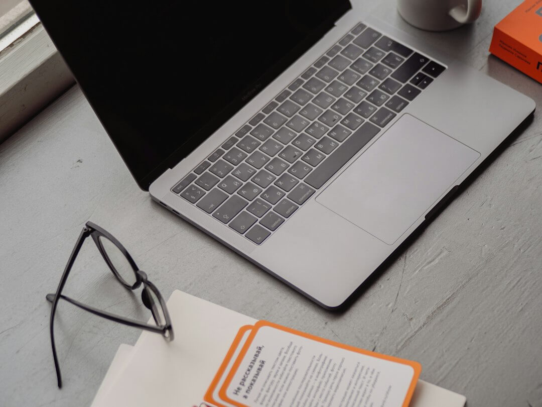 macbook pro beside black framed eyeglasses and white ceramic mug